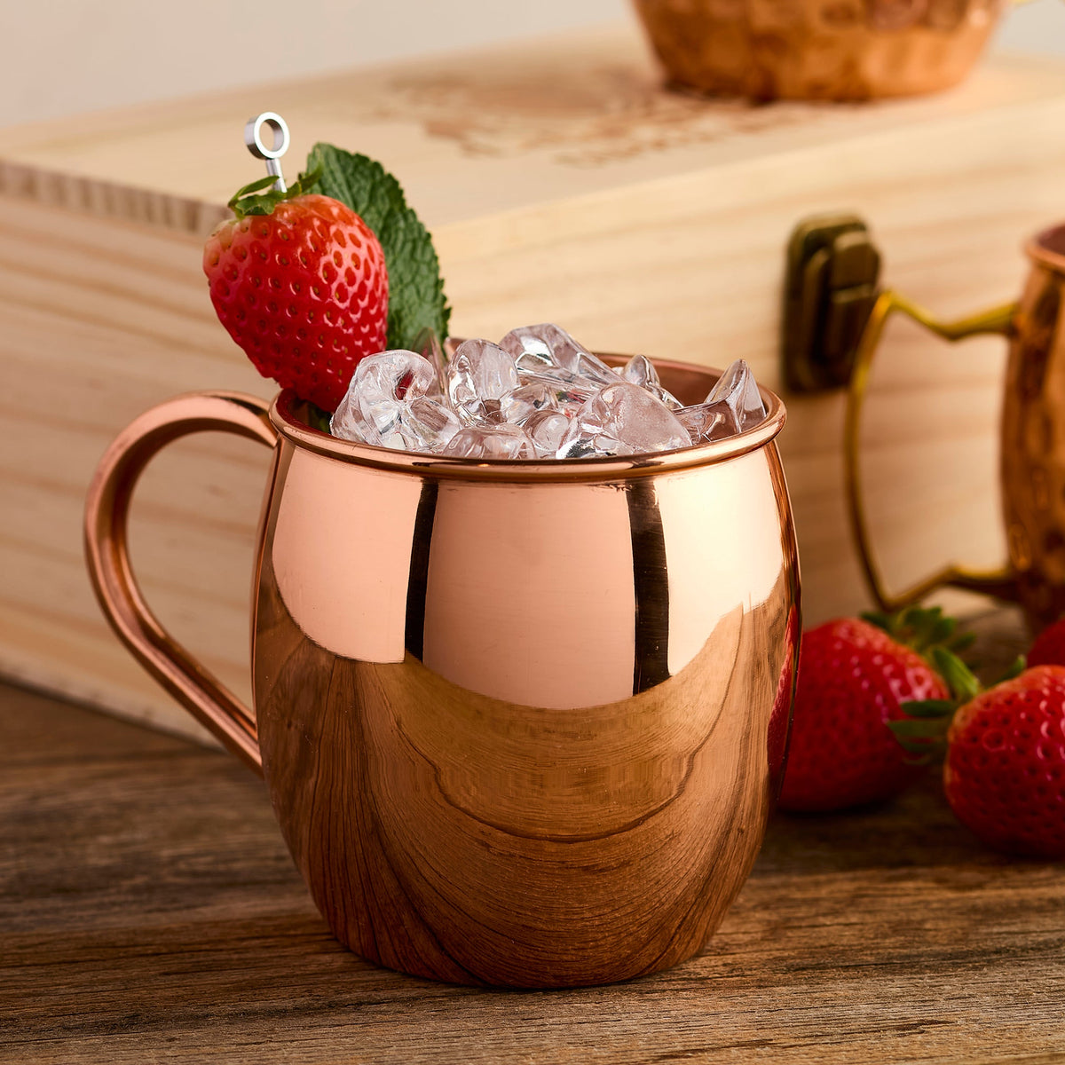 Solid copper mugs with ice and strawberries on a wooden surface