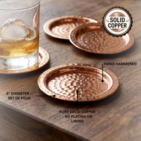 Four hammered solid copper coasters on a wooden table, with one coaster supporting a glass of whiskey. Text labels mention 4-inch diameter, set of four, hand hammered, pure solid copper, and no plating or lining.