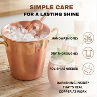A copper bucket with smooth surface filled with ice on a wooden table, alongside copper mugs and care instructions text reading handwash only, dry thoroughly, and polish as needed.