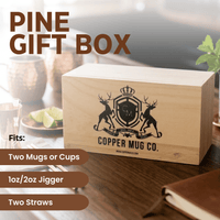 A light natural wood gift box engraved with the Copper Mug Co. crest and text, shown on a wooden table in a styled setting.