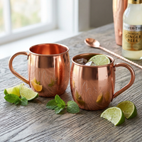 Two copper Moscow mule mugs with handles sit on a rustic wooden table with engraving of Mr and Mrs.