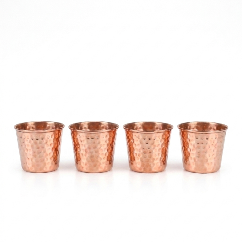 Four small hammered copper tumblers arranged in a row on a clean white background.