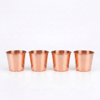Four small copper-colored metal tumblers lined up in a row on a plain white background.